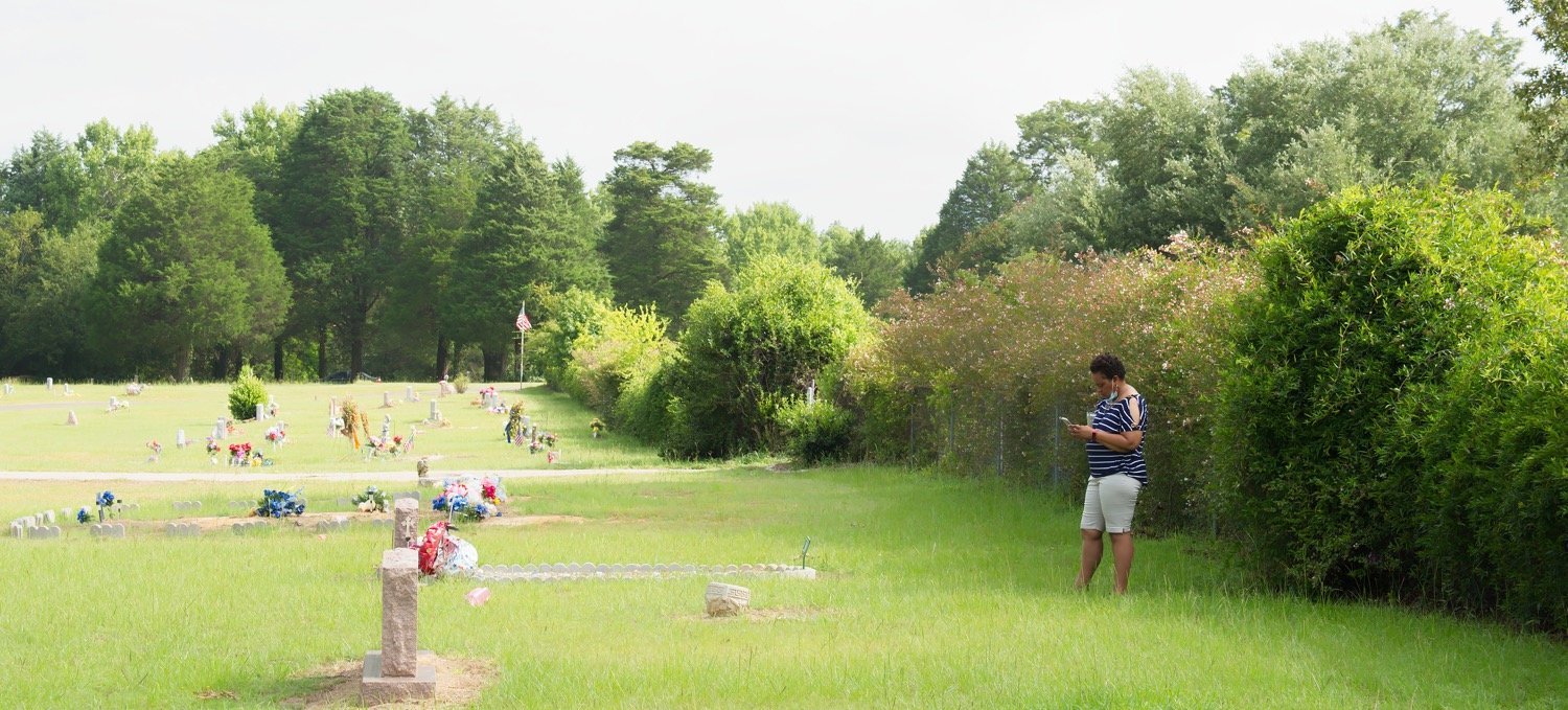 Gildred Price Barber, with the cemetery fence/boundary in the background, checks on her mother’s grave in the west section (See photos from before and after the fence was removed).